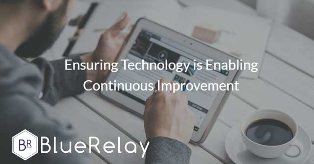 Image of a bearded man in a grey hoodie using a tablet, with a coffee on the table he is sitting near