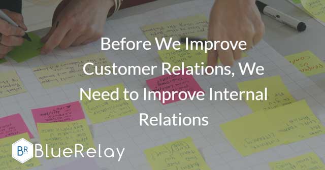 Image of two sets of hands, one writing on different coloured post-it notes, and the other putting them onto a white board laying flat on a table