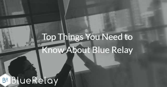 Photo of a man with short black hair and medium rimmed black glasses writing on a whiteboard