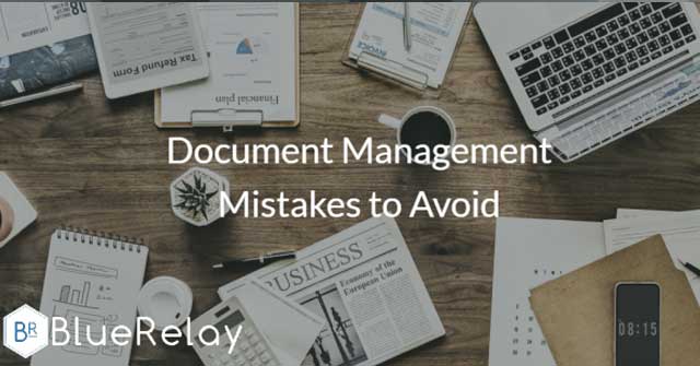 Photo of the top of a wooden table with a variety of clipboards, newsparpers, and notepads on it, along with a mobile phone, coffee mug, and laptop, all scattered across the table